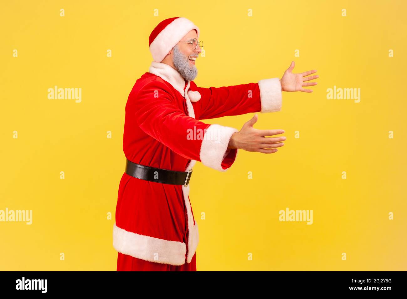 Vista laterale dell'anziano egoista con barba grigia indossando il costume di babbo natale in piedi con le braccia sollevate, pronto a abbracciare, incontro. Studio interno sh Foto Stock