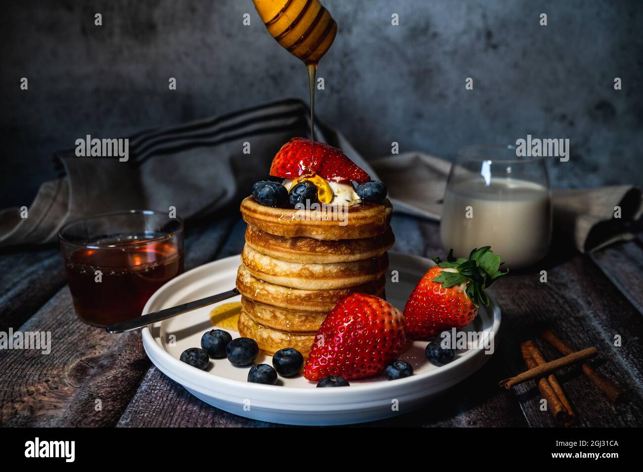 Una pila di pancake con miele versante, mirtillo e fragola e panna di frusta sul piatto su tavola di legno, delizioso dessert per la colazione Foto Stock