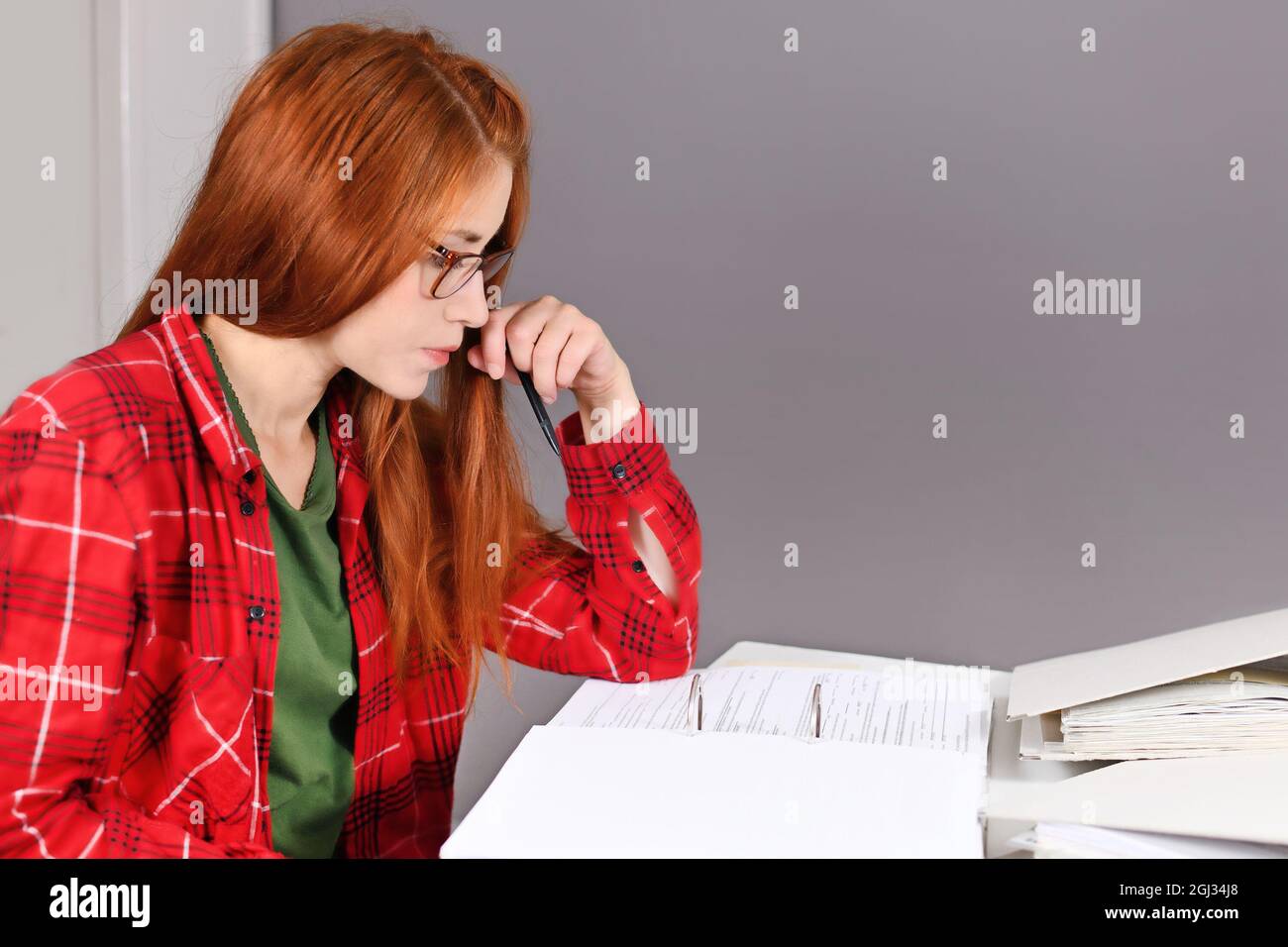 Donna con capelli rossi seduti alla scrivania guardando il documento nella lima ad anello Foto Stock