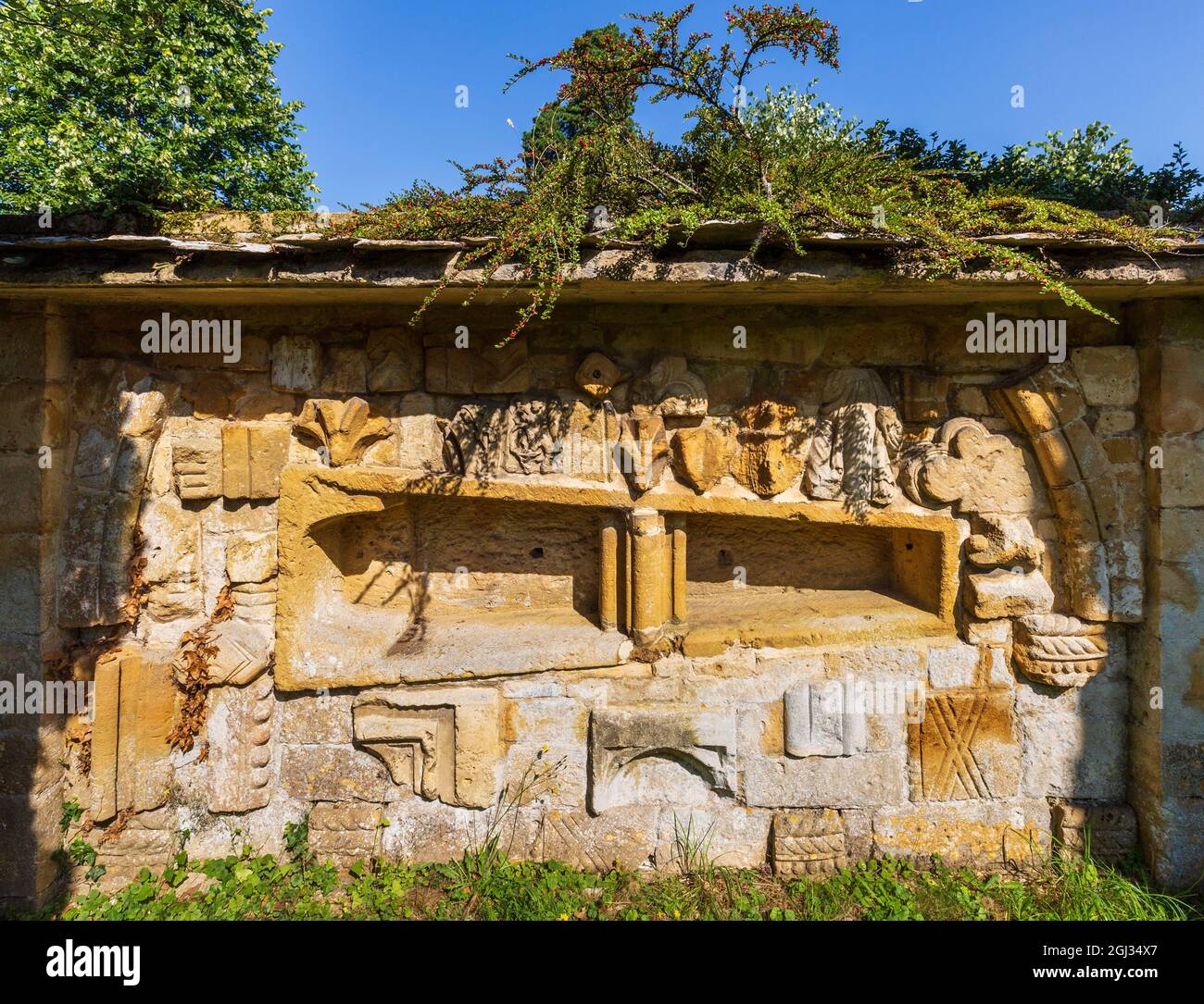 Frammenti della pietra intagliata dall'Abbazia di Hailes incastonati nel muro del cimitero della chiesa di San Pietro vicino a Stanway House, Cotswolds, Inghilterra Foto Stock