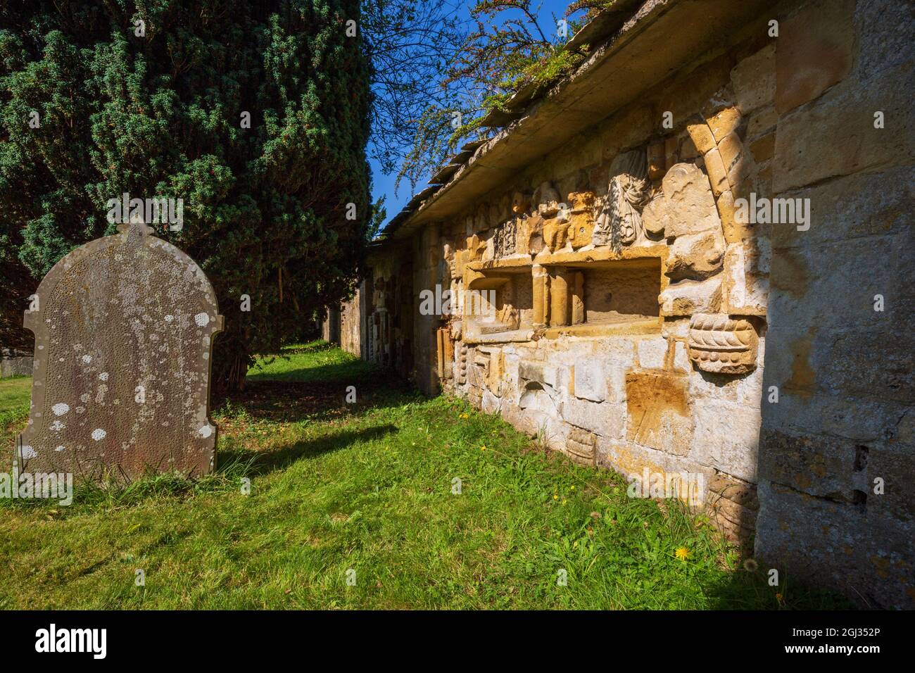 Frammenti della pietra intagliata dall'Abbazia di Hailes incastonati nel muro del cimitero della chiesa di San Pietro vicino a Stanway House, Cotswolds, Inghilterra Foto Stock