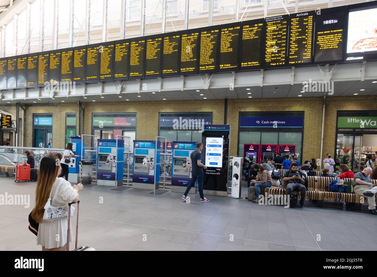 Viaggio in treno nel Regno Unito; una donna passeggero che guarda il bordo di partenza del treno, stazione di Kings Cross, Londra, Regno Unito Foto Stock