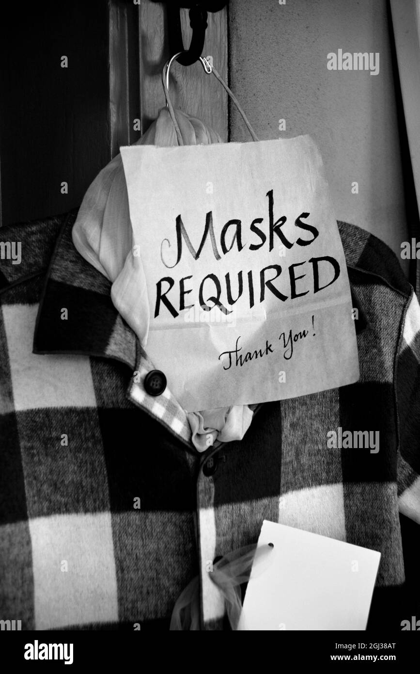 Un cartello all'esterno di un negozio di abbigliamento informa i clienti che all'interno del negozio sono necessarie maschere per il viso. Foto Stock
