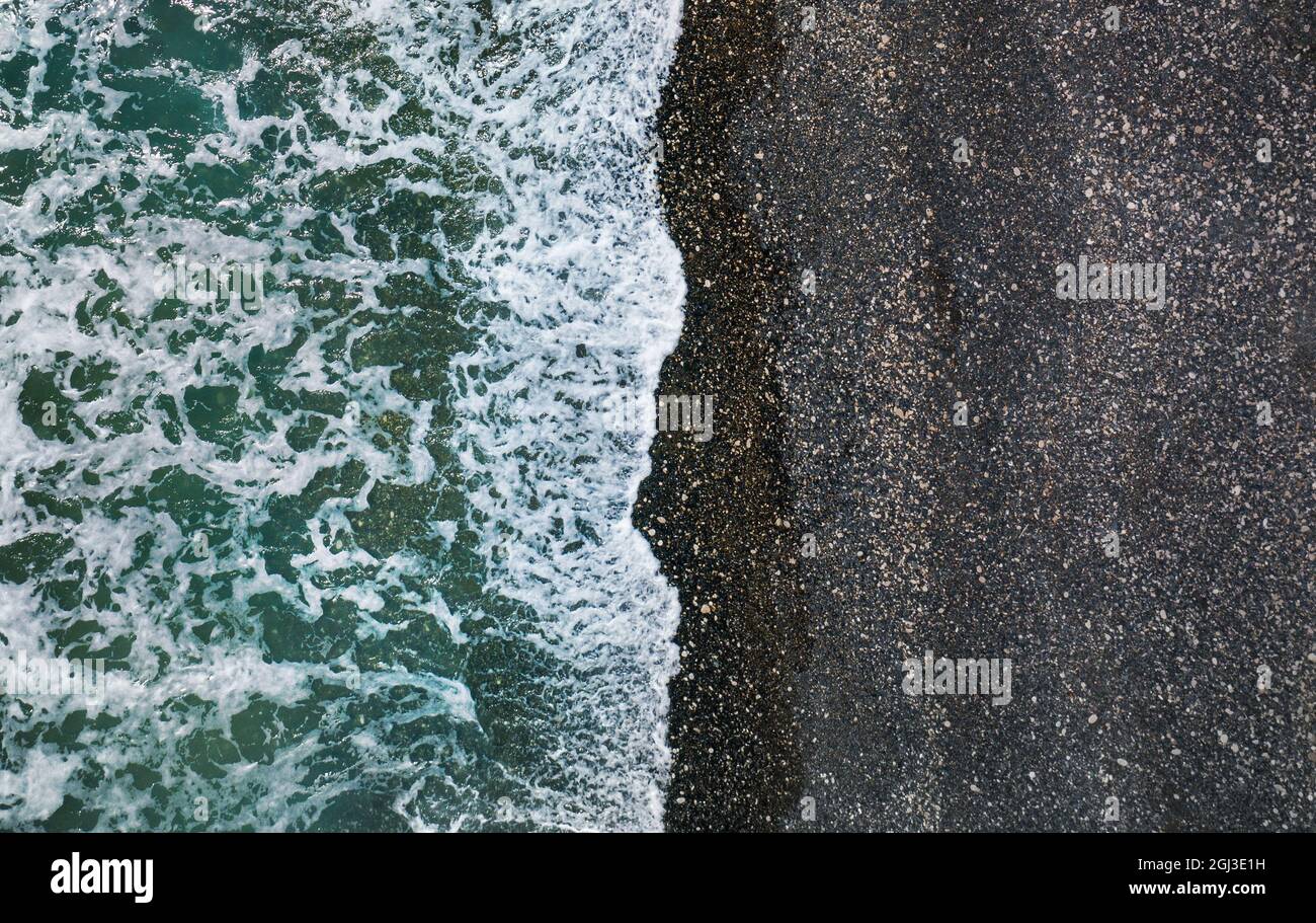 Onde di mare che si infrangono su una spiaggia selvaggia con sabbia nera e ciottoli, sfondo naturale aereo Foto Stock