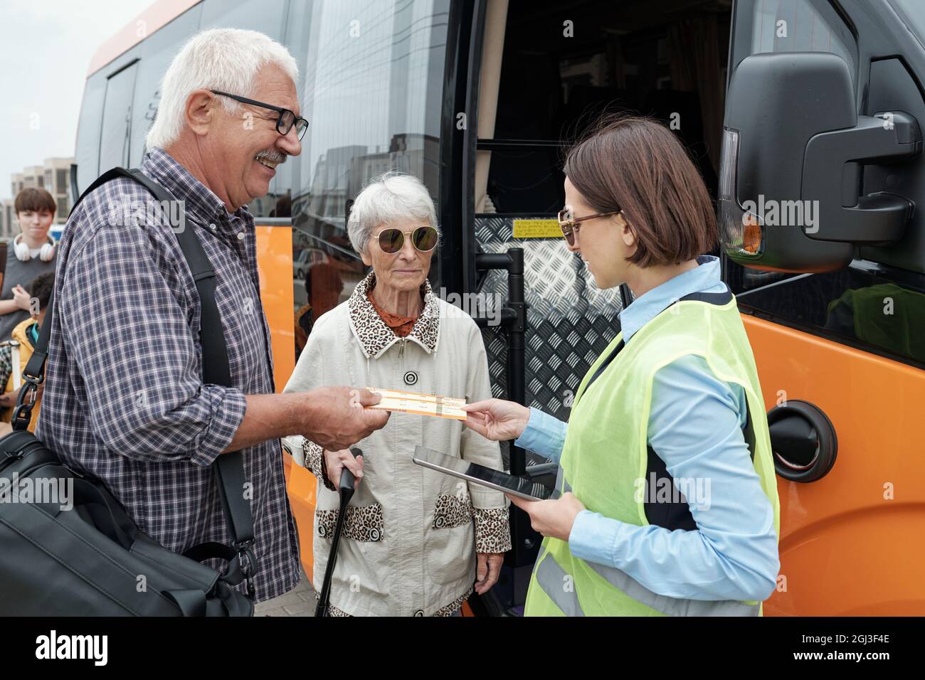 Coppia caucasica senior in piedi alla porta aperta dell'autobus e mostrando i biglietti per il supervisore dell'autobus con tablet Foto Stock