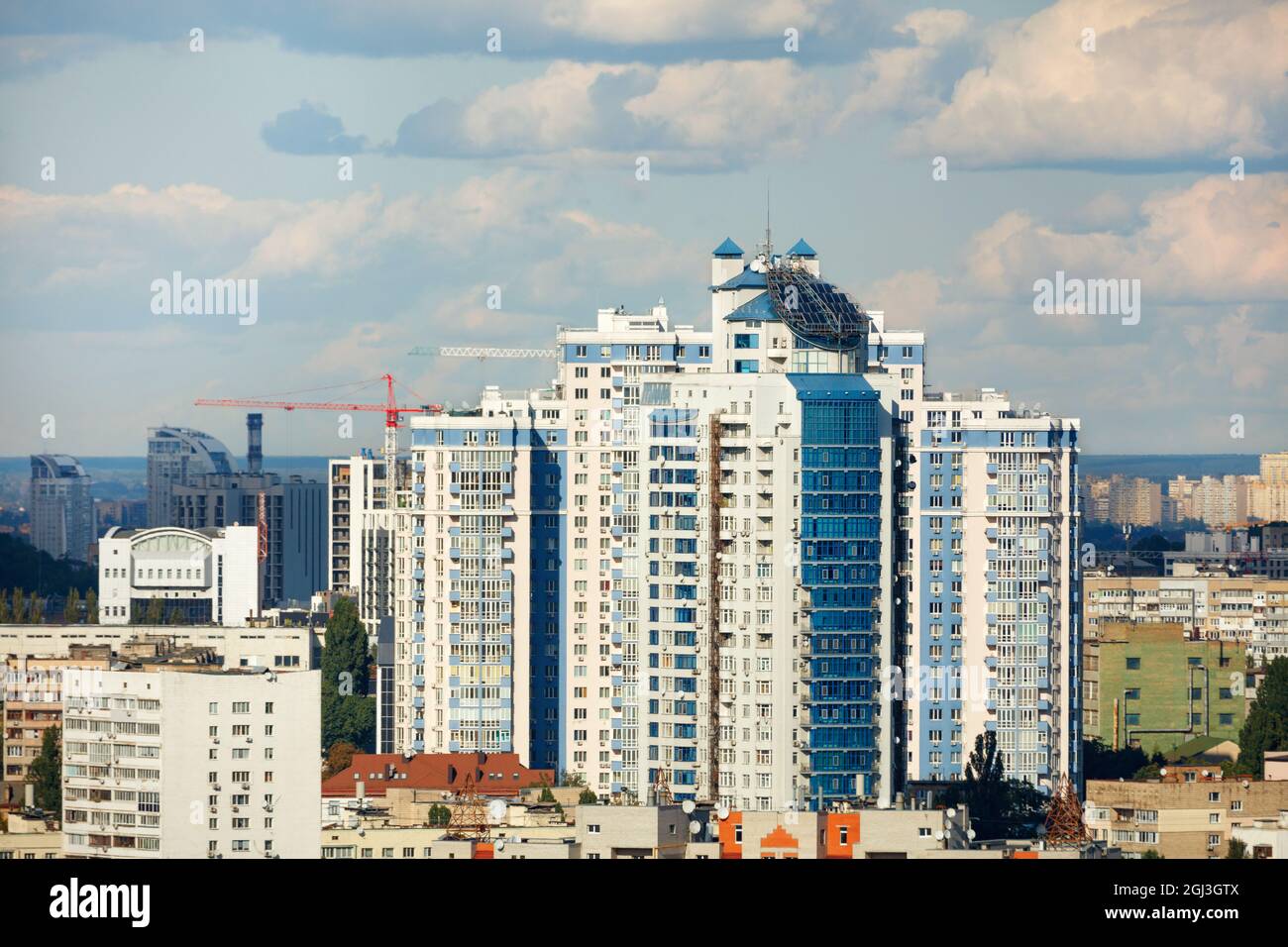 Pannelli solari sul tetto di un edificio a più piani sullo sfondo di una zona residenziale della città con un cielo blu nuvoloso in una calda giornata estiva. Foto Stock