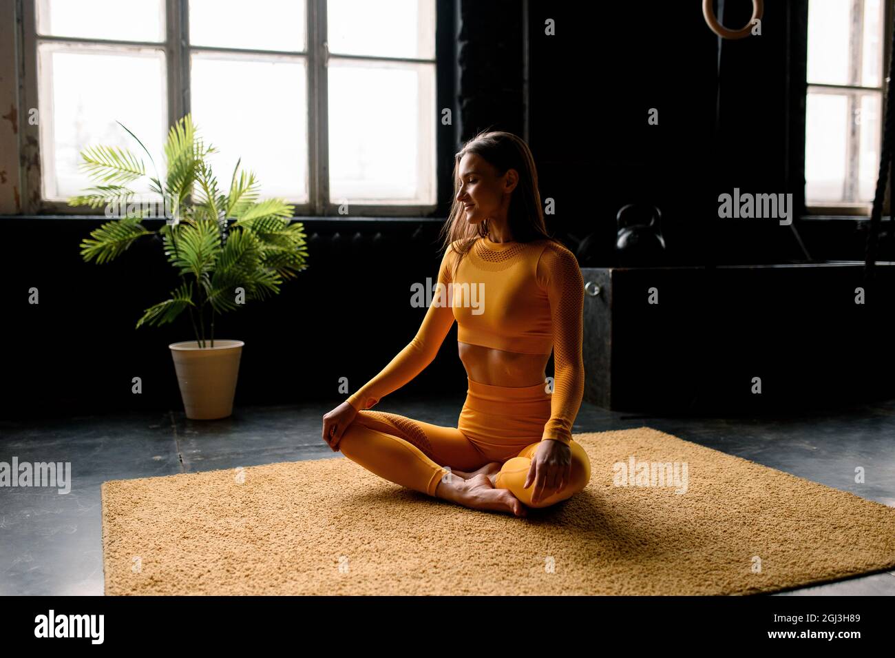 bella ragazza in uno sport giallastro sta facendo in yoga, respirando correttamente. Moderna sala sportiva Foto Stock