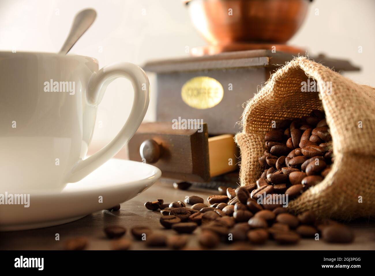 Tazza di caffè con sacco pieno di chicchi e macinacaffè manuale su tavola di legno dettaglio. Vista frontale. Composizione orizzontale. Foto Stock