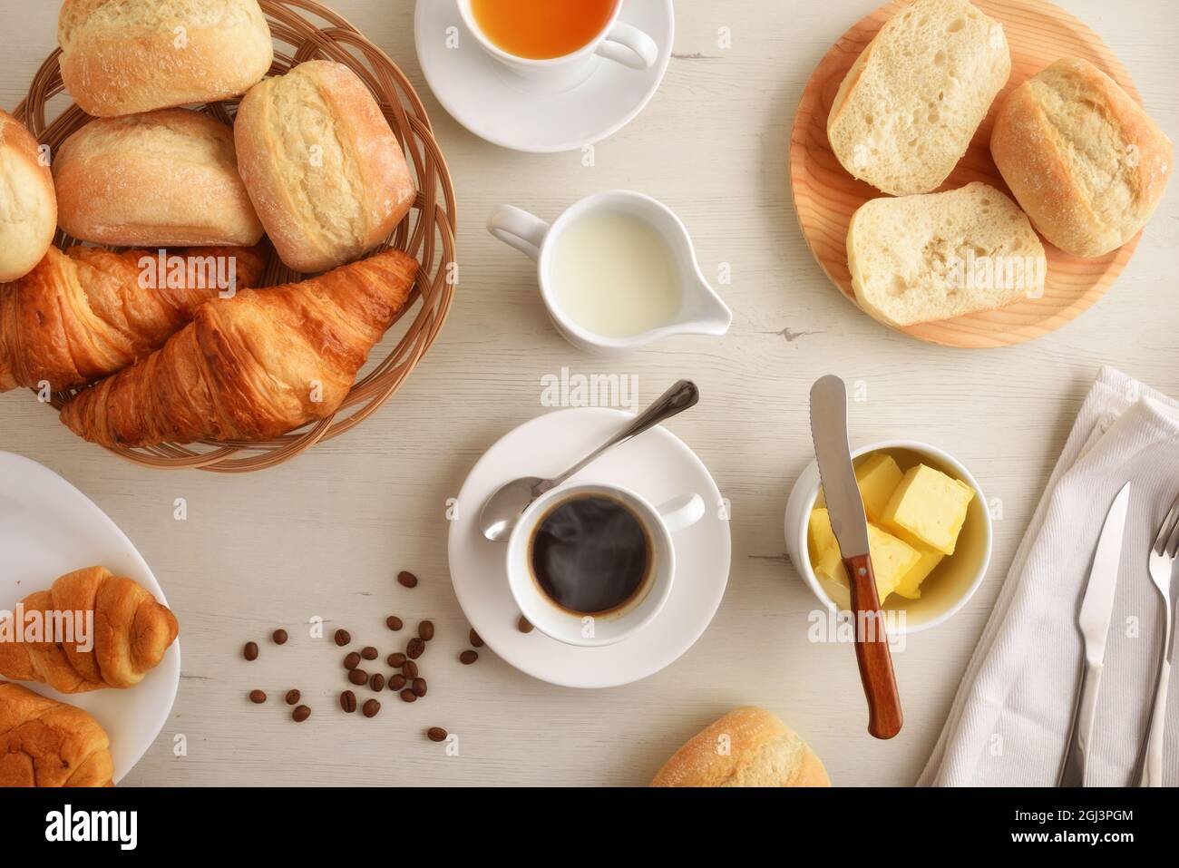 Caffè del mattino su un tavolo di legno bianco con piatto con due croissant e pane con fondo bianco isolato. Vista frontale. Composizione orizzontale. Foto Stock