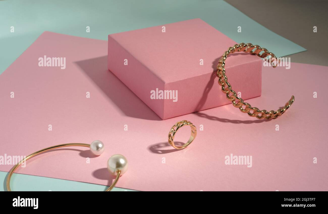 Bracciale a catena dorato e anello su sfondo di carta rosa e verde con spazio per la copia Foto Stock