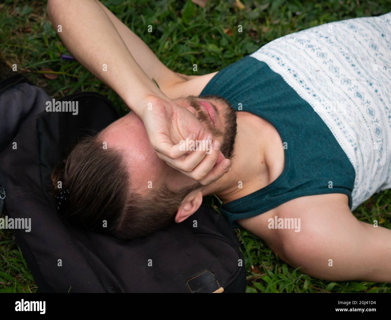 L'uomo bianco si trova sull'erba coprendo il viso con il braccio Foto Stock