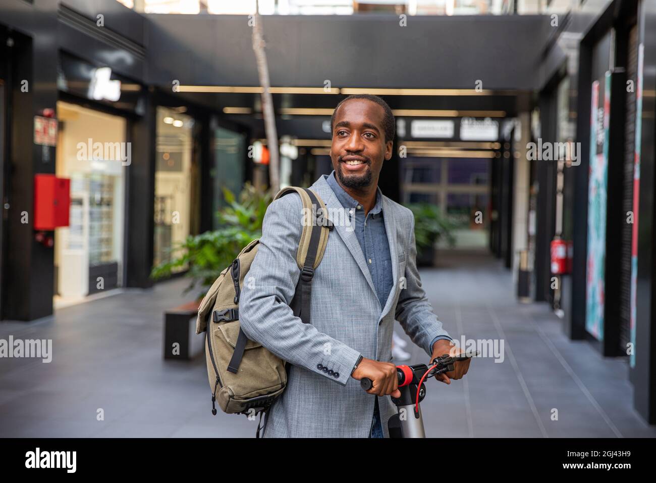 Uomo d'affari africano con il suo scooter elettrico. Il ragazzo sorridente vestito elegantemente va a lavorare con un veicolo non inquinante - concetto di mobilità pulita Foto Stock