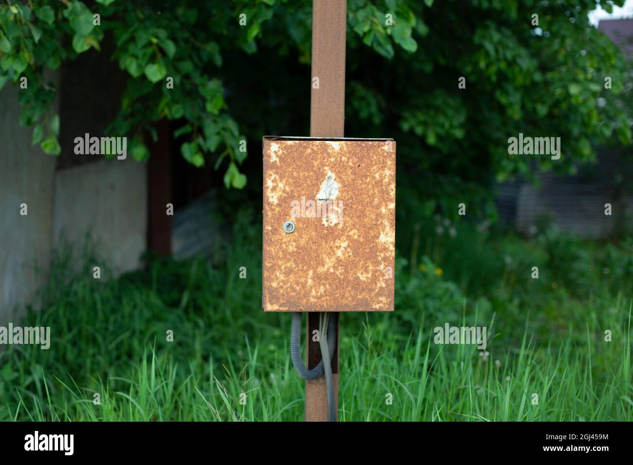 Una scatola arrugginita su un palo. La scatola è sospesa nel villaggio. Vecchio quadro elettrico. Luogo di controllo della tensione elettrica. Foto Stock
