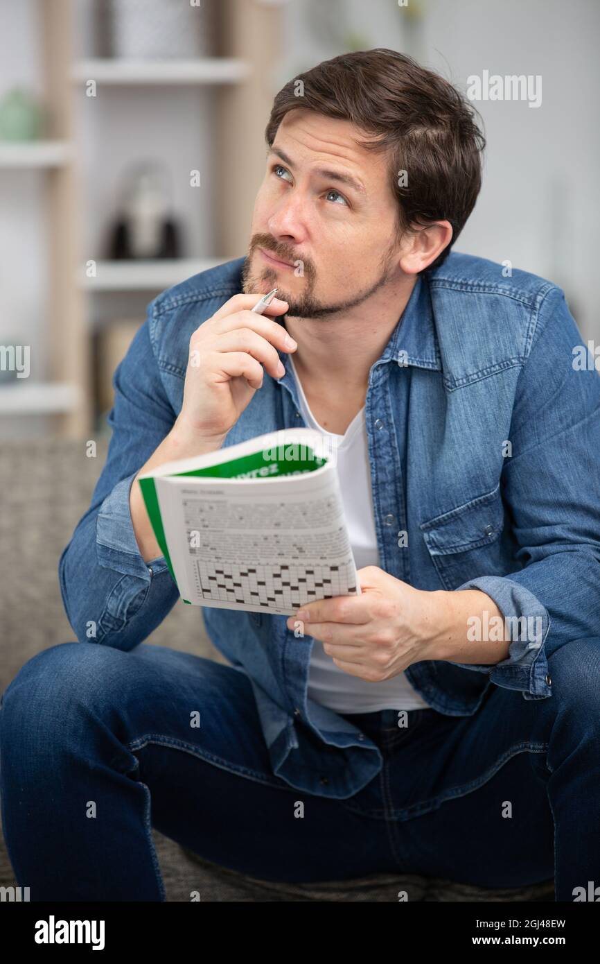 giovane uomo seduto facendo un puzzle crossword guardando pensieroso Foto Stock
