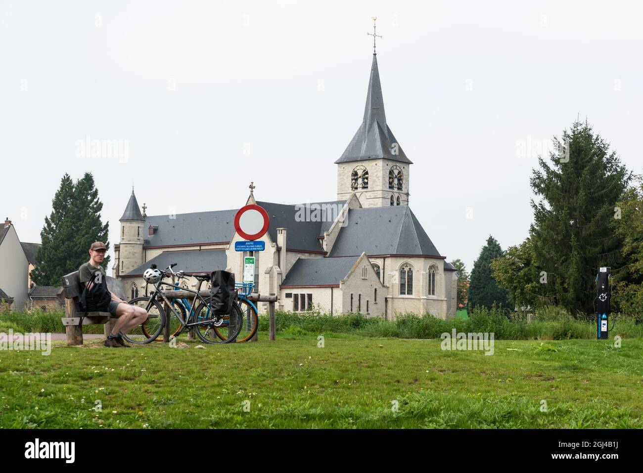 Vilvoorde, Brabante fiammingo - Belgio - 09 01 2021: Uomo che riposa con il suo bicilo con una chiesa bianca e verde circostante sullo sfondo Foto Stock