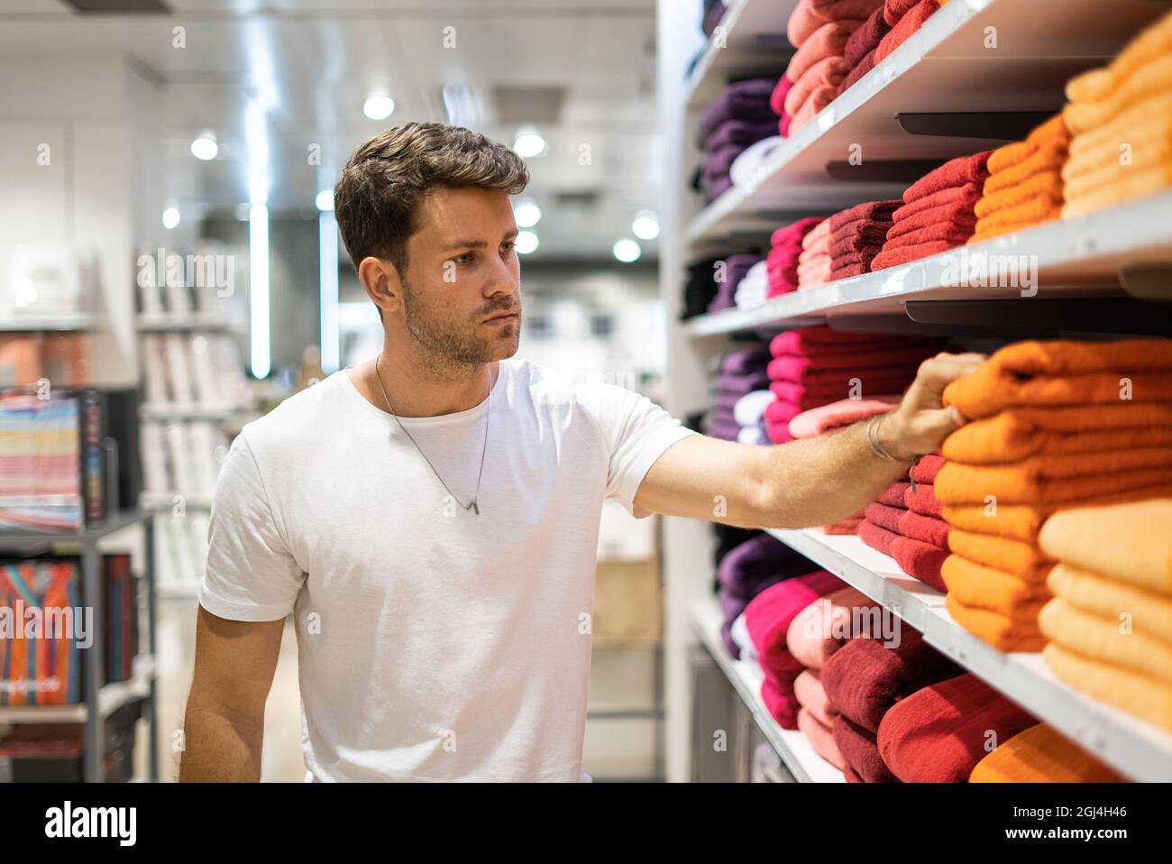 Giovane cliente maschio bearded che sceglie gli asciugamani colorati luminosi dallo scaffale mentre visita il reparto domestico delle merci nel negozio moderno Foto Stock
