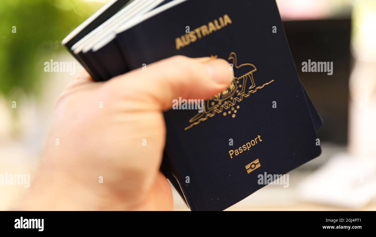 Una mano volutamente sfocata che stringe una grande quantità di passaporti australiani. Grande vacanza familiare internazionale. Restrizioni di blocco di sfuggita e b Foto Stock