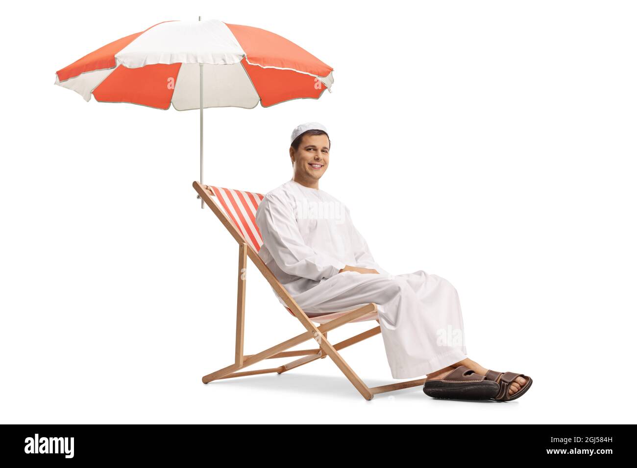Giovane uomo in abiti etnici seduto su una sedia da spiaggia sotto ombrello isolato su sfondo bianco Foto Stock