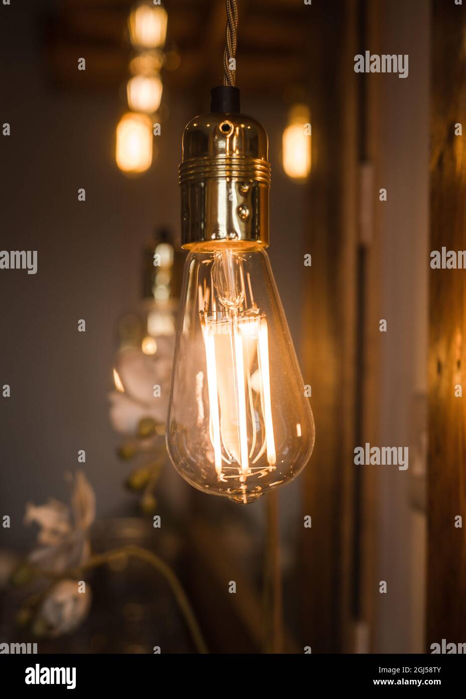 Grande vecchia lampadina elettrica arancione calda incandescente industriale appesa con altre sullo sfondo. Luminescenza retrò scuro con elemento decorativo vintage luminoso Foto Stock