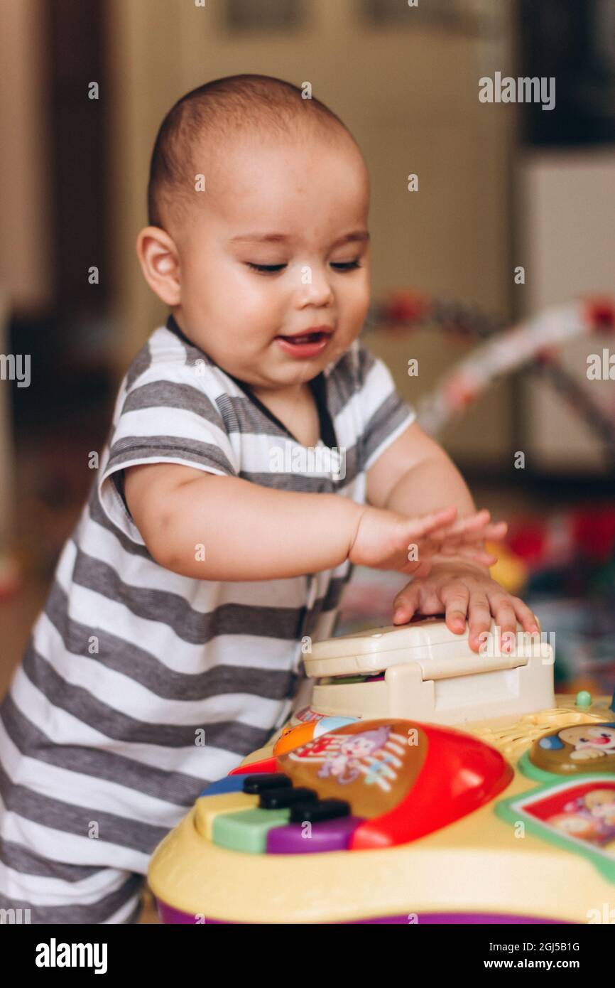 Simpatico baby chubby si alza e gioca con il tavolo di musica per bambini. Un sacco di giocattoli colorati ovunque. Foto Stock