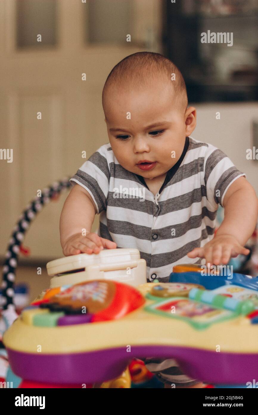 Simpatico baby chubby si alza e gioca con il tavolo di musica per bambini. Un sacco di giocattoli colorati ovunque. Foto Stock