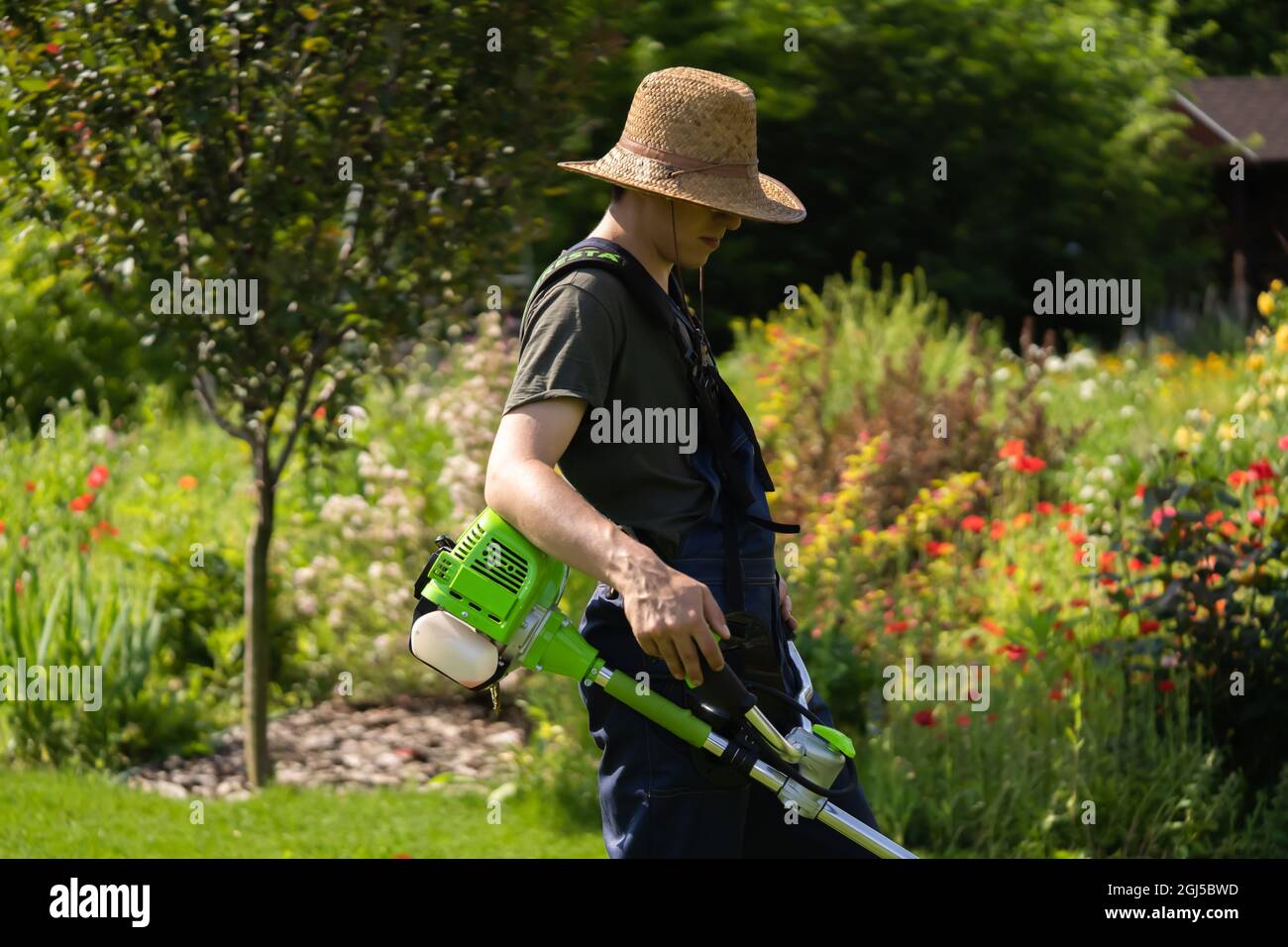 Un giovane uomo con un rasaerba si prende cura dell'erba nel cortile. Foto Stock