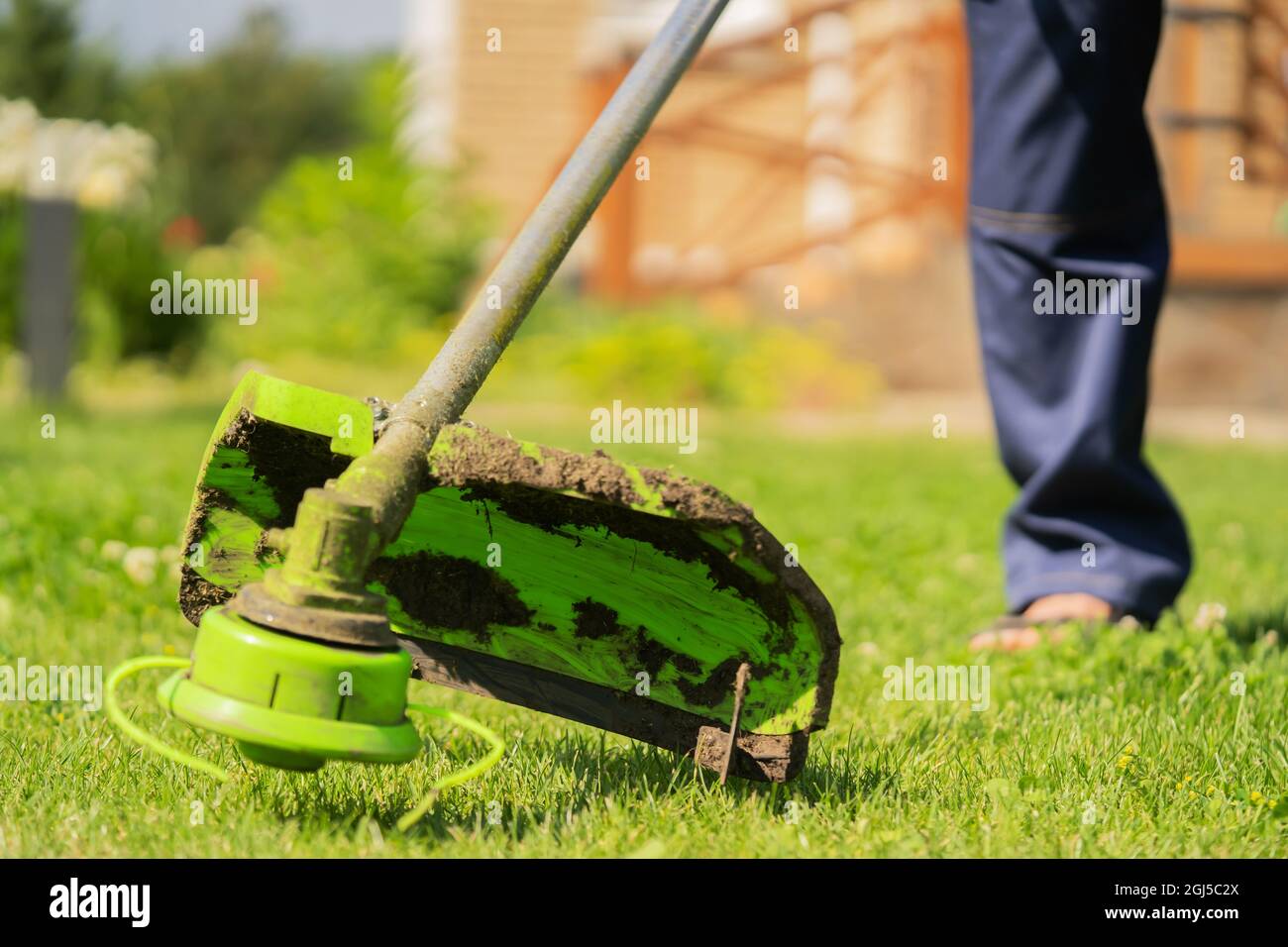 Un primo piano di un giovane uomo con un tosaerba che si prende cura dell'erba nel cortile. Foto Stock