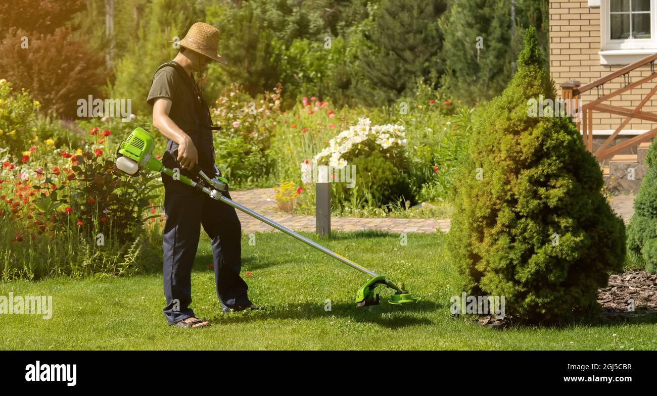 Un giovane uomo con un rasaerba si prende cura dell'erba nel cortile. Foto Stock