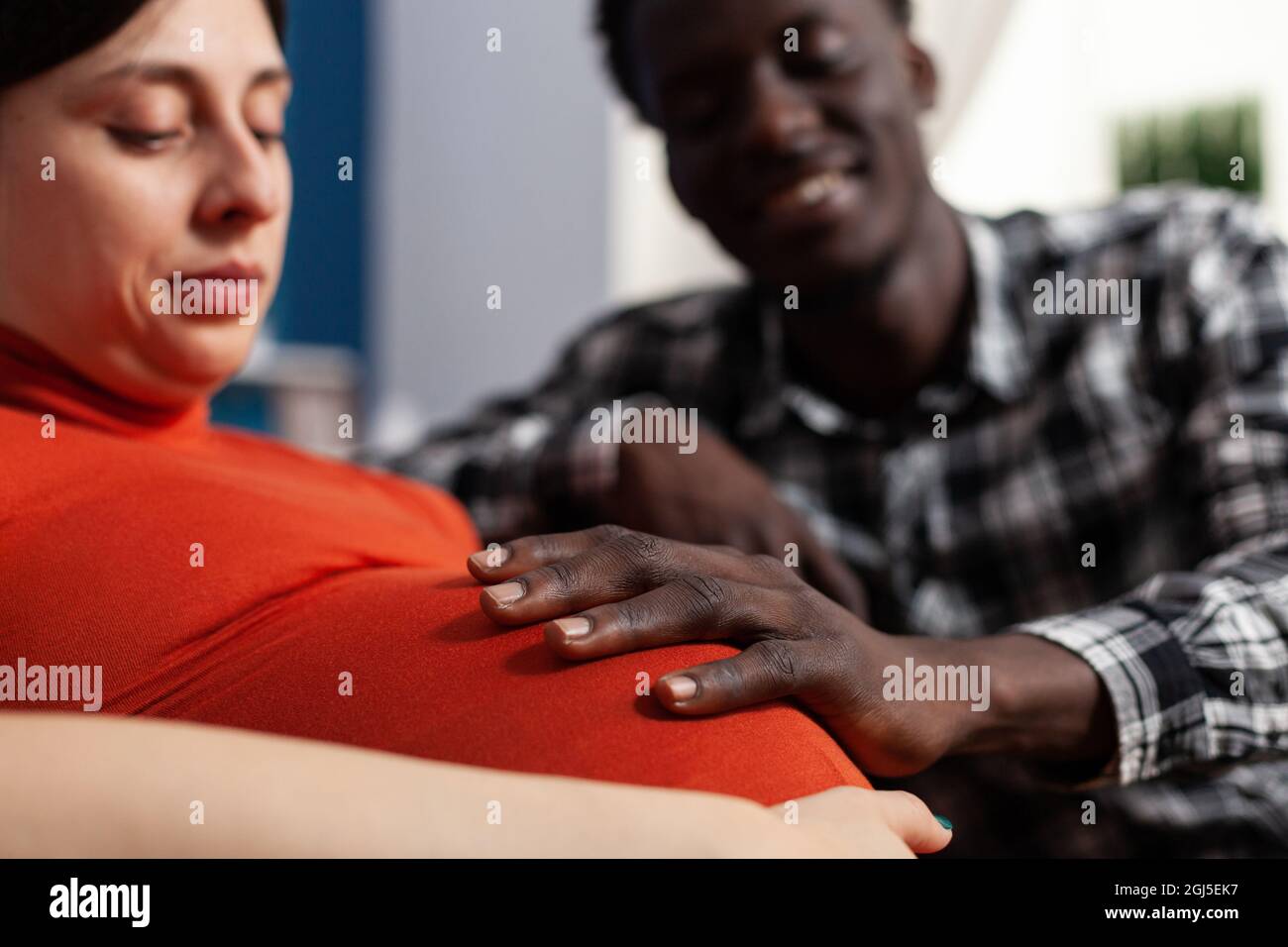 Primo piano del padre nero del bambino che tocca il ventre della donna incinta. L'uomo afroamericano che tiene la mano sul bump del bambino sorridendo circa la paternità. Coppia interrazziale con gravidanza. Foto Stock
