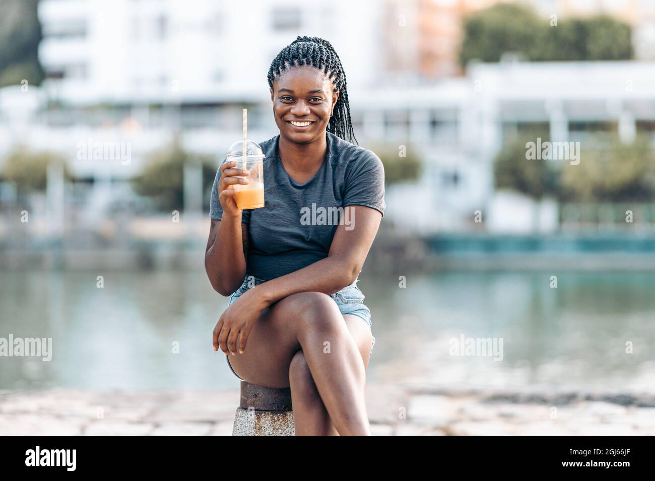 Donna africana seduta mentre tiene una vibrazione e sorride alla macchina fotografica all'aperto Foto Stock