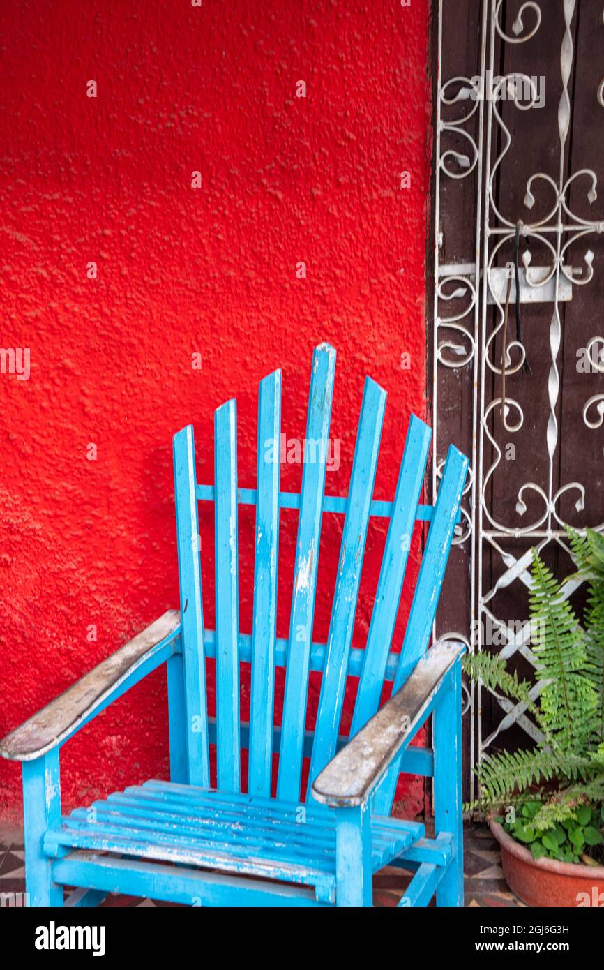 Una sedia blu a tempo Adirondack di fronte al muro rosso di stucco a LaBoca, Cuba. Foto Stock