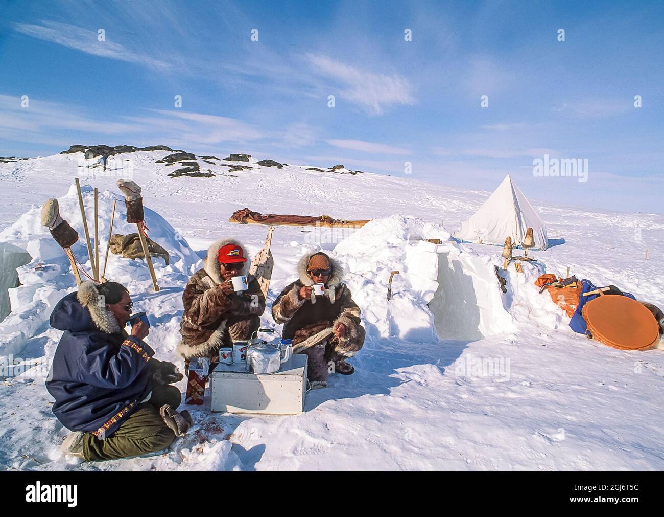 Lago Baker, Nunavut, Canada. Gli uomini inuit siedono fuori i loro igloos sorseggiando il tè caldo. Gli stivali possono essere visti in aria, insieme a una tenda e slitta tradizionale Foto Stock