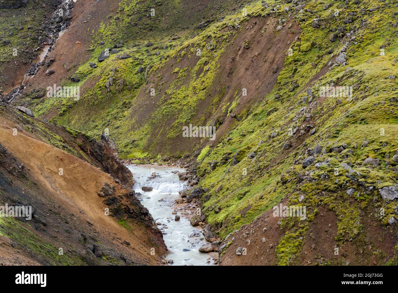 Islanda, Highlands meridionali, Monti Kerlingarfjoll. Un ruscello glaciale taglia la pietra rossa della rhyolite vulcanica che è coperta di grée brillante Foto Stock