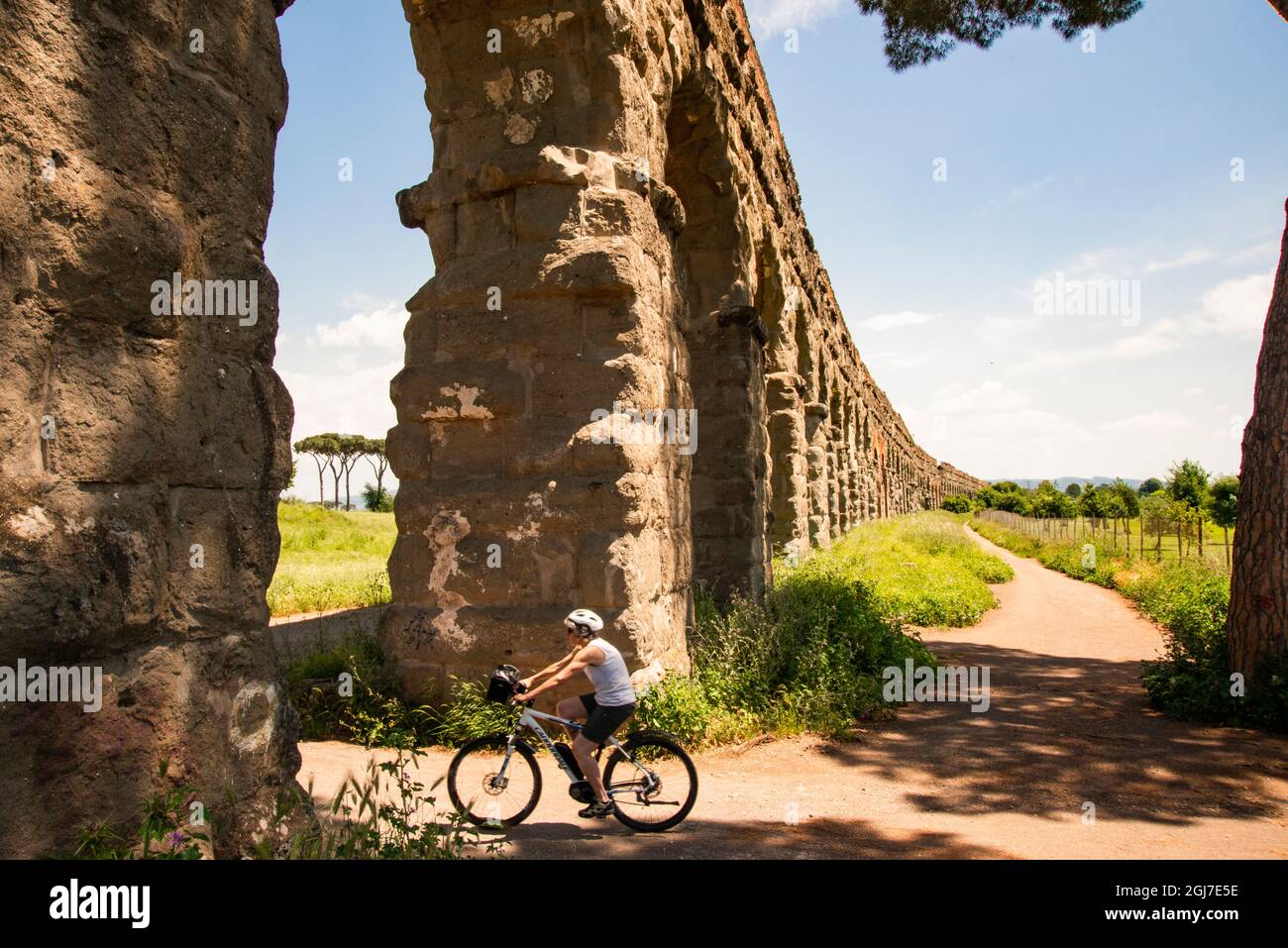 Italia, Roma. Parco Regionale Via Appia, Antica, Roma Vecchio, bicyclist passando sotto l'arco di Aqua Claudio. Foto Stock