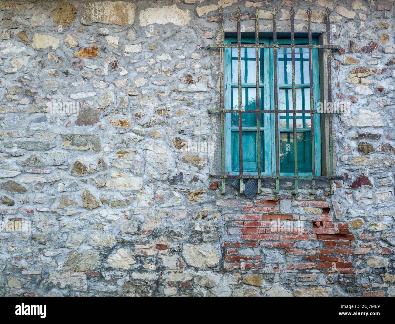 Italia, Toscana. Finestra turchese con sbarre su vecchia casa di pietra. Foto Stock