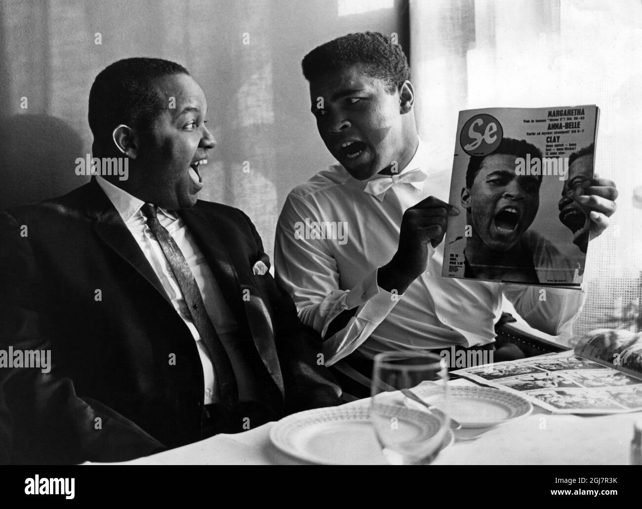 Il campione del mondo di boxe Muhammad Ali è visto mostrare una copertina di una rivista svedese per il suo consigliere Herbert Muhammed a Stoccolma, Svezia 1965. Ali era in Svezia per la lotta in mostra. Foto Stock