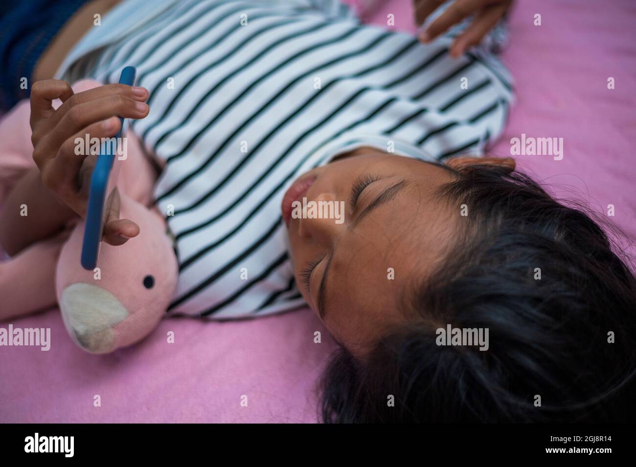 Ragazza asiatica che guarda il contenuto sul suo letto al mattino utilizzando uno smartphone Foto Stock