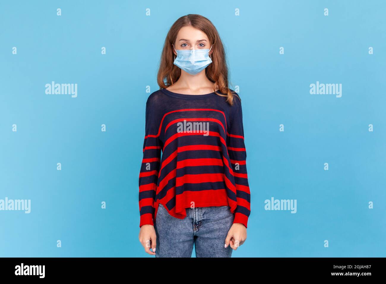 Donna stretty che indossa a strisce stile casual maglione e maschera igienica per prevenire l'infezione, malattie respiratorie come influenza, coronavirus. Per interni Foto Stock