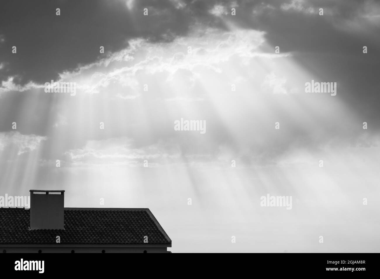 Raggi di luce dal sole chiamati raggi crepuscolari tetto della casa. Fascio di luce e nuvole nel cielo. Foto Stock