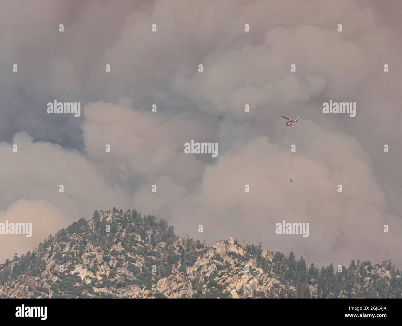 Elicottero antincendio con secchio d'acqua che vola nelle nuvole di fumo e fuoco dal fuoco selvatico a Black Mountain, Southern Sierra Nevada Mountains, California, Fro Foto Stock