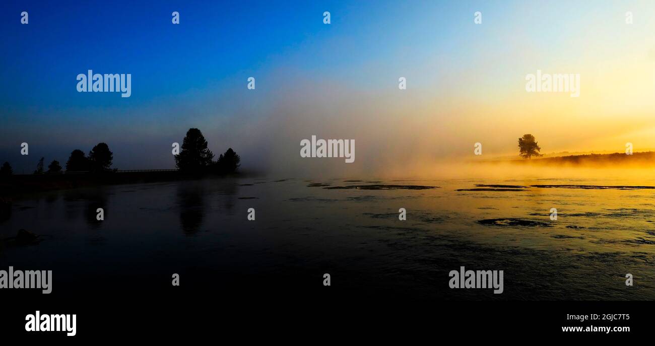 Alba del mattino con alberi e fiume sotto il cielo blu e la nebbia incandescente Foto Stock