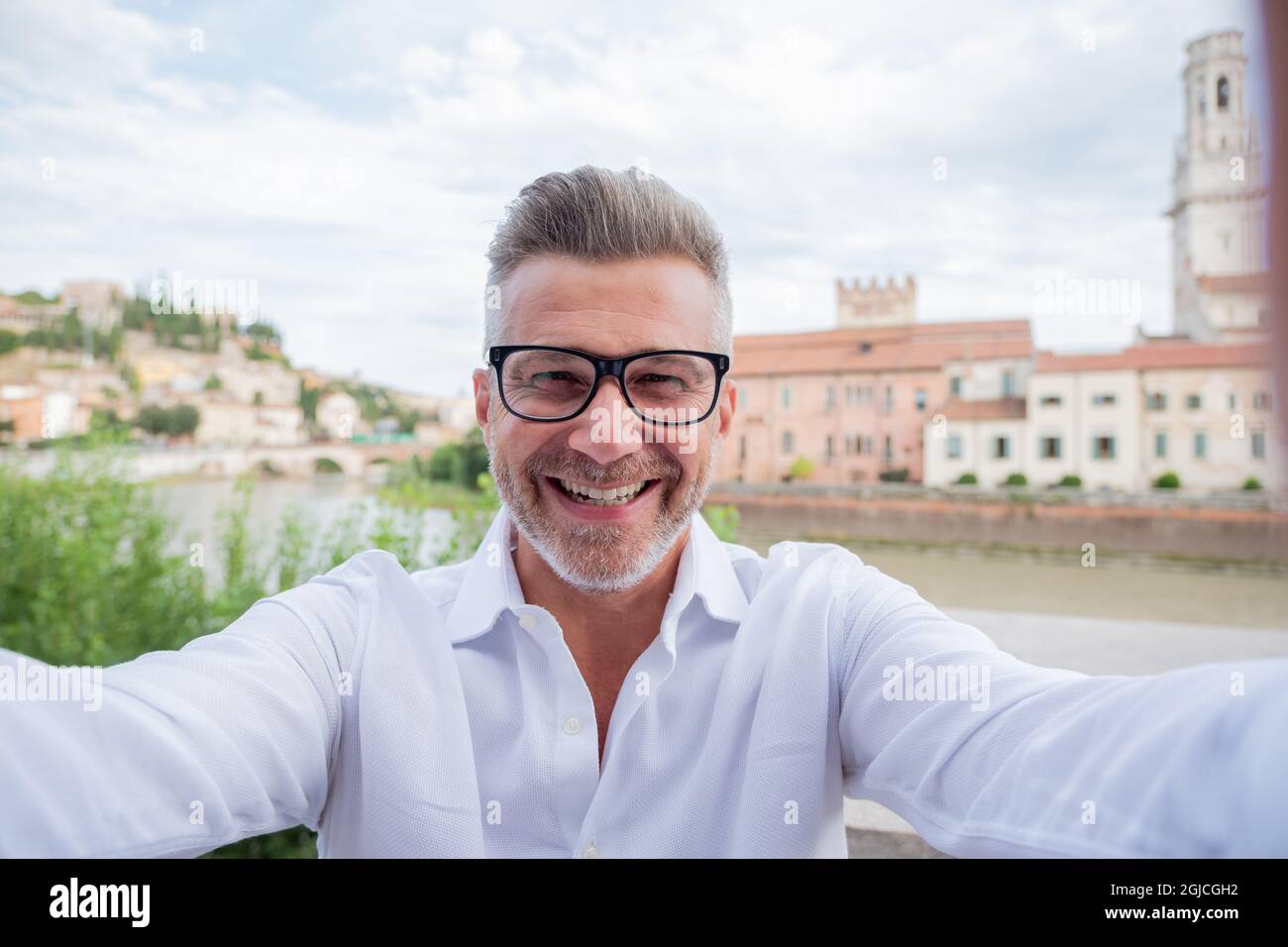 Primo piano o ritratto di ottimista grigio capelli uomo d'affari facendo selfie sorridente e indossare occhiali camicia bianca all'aperto in città Foto Stock