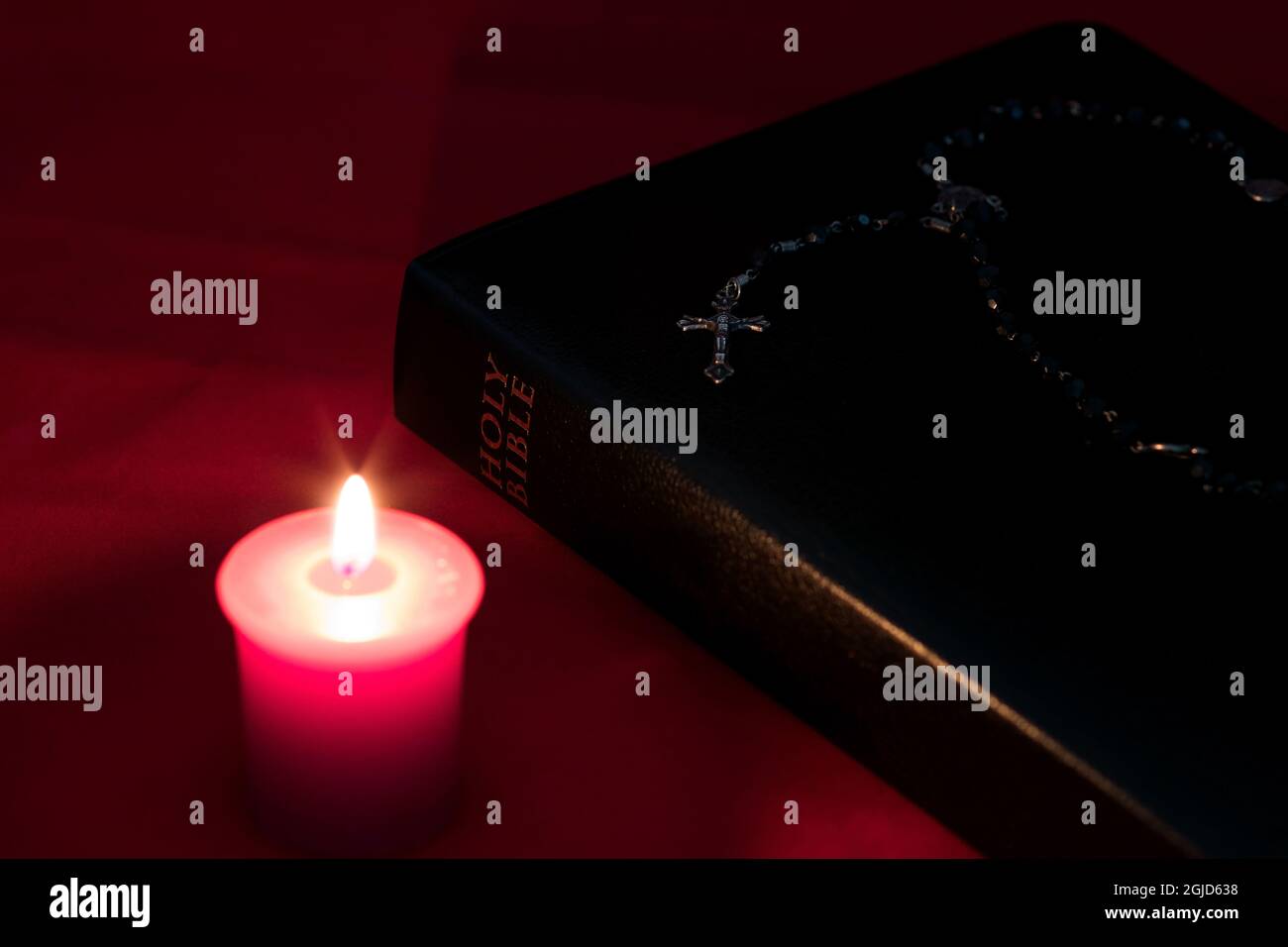 Bibbia con candela e rosario su un panno rosso da tavola Foto Stock