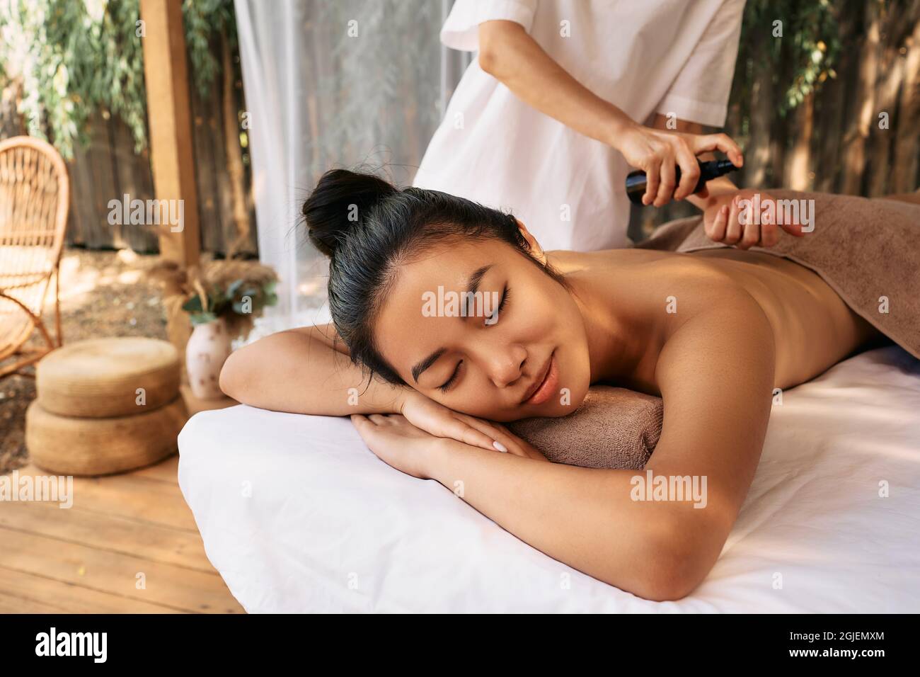 Il massaggiatore applica l'olio aromatico al corpo della giovane donna asiatica durante il massaggio e l'aromaterapia nella splendida spa del resort Foto Stock