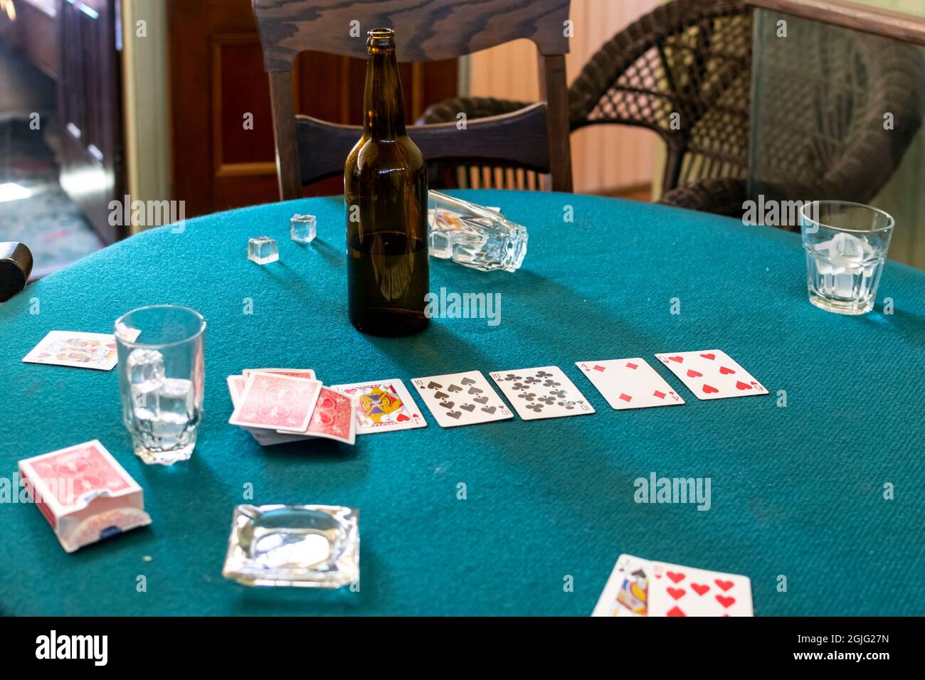 Una mezza bottiglia vuota di birra si indossa su un tavolo di carte d'epoca con bicchieri di ghiaccio, un posacenere e un mazzo di carte, dopo una partita. Foto Stock
