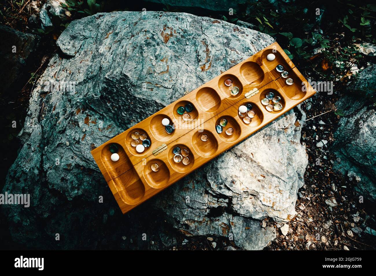 Tradizionale gioco di tavolo di Mancala con pezzi di vetro sul percorso di roccia all'esterno Foto Stock