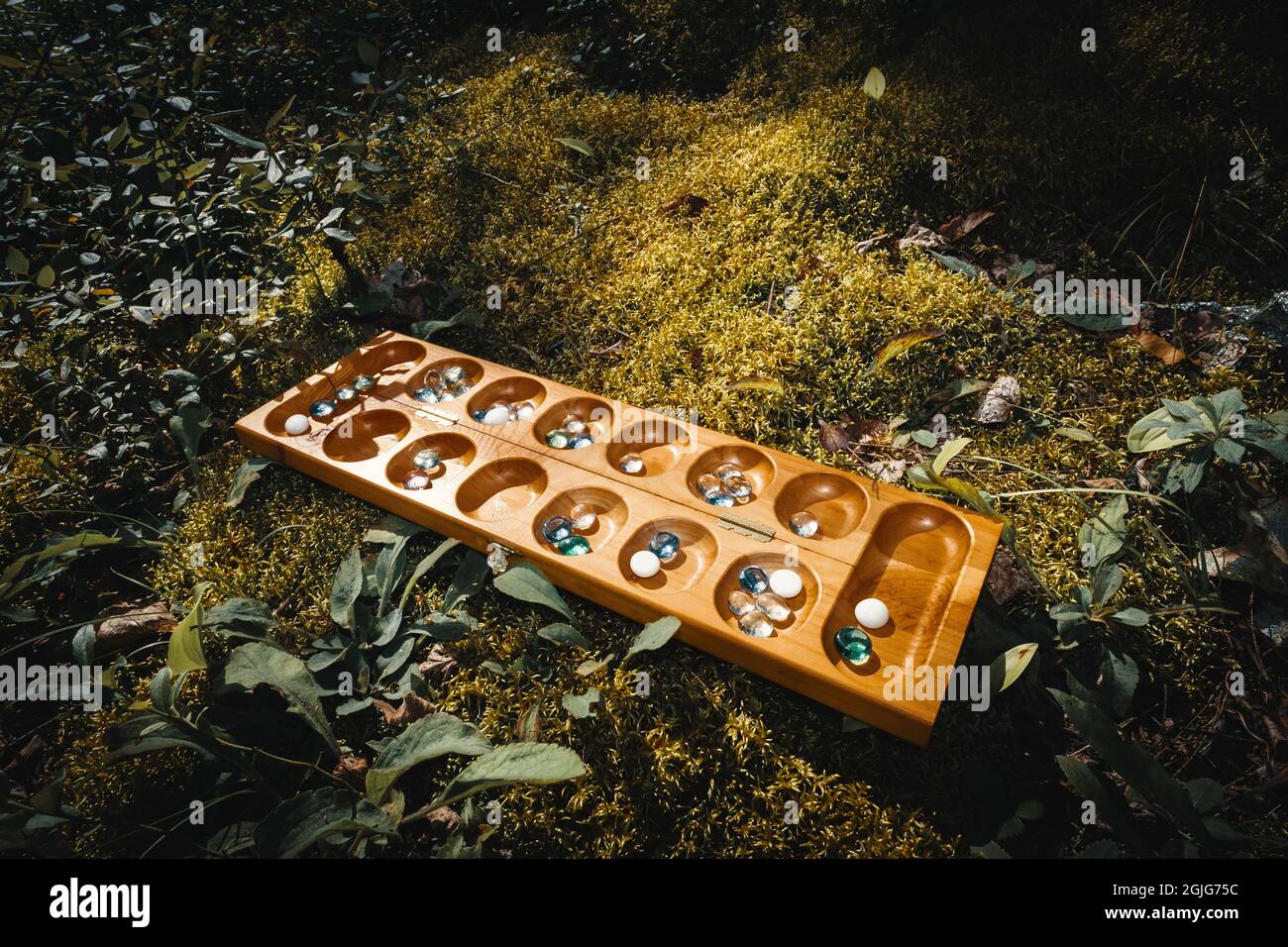 Tradizionale gioco di tavolo Mancala con pezzi di vetro sul letto di muschio all'esterno Foto Stock