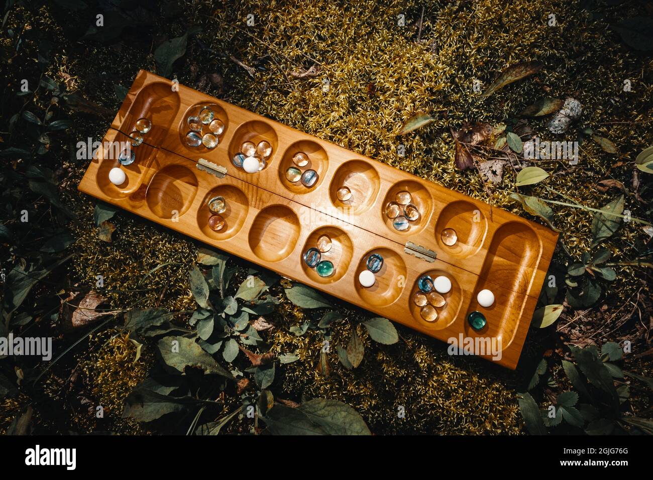 Tradizionale gioco di tavolo Mancala con pezzi di vetro sul letto di muschio all'esterno Foto Stock