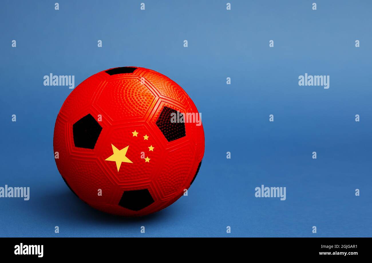 Pallone da calcio dipinto in colori di bandiera cinese su sfondo blu Foto Stock
