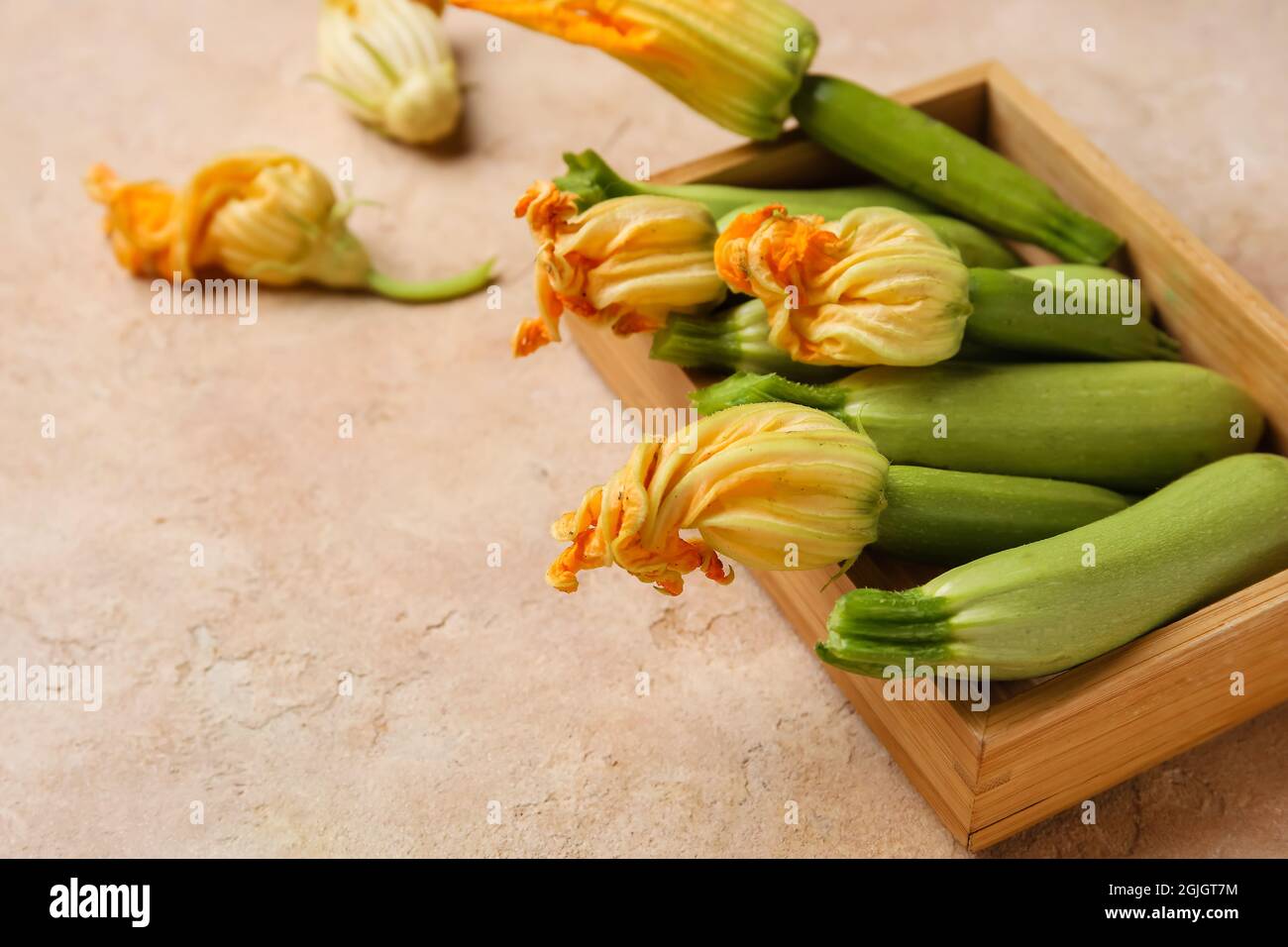 Scatola in legno con zucchine fresche e fiori su sfondo colorato Foto Stock